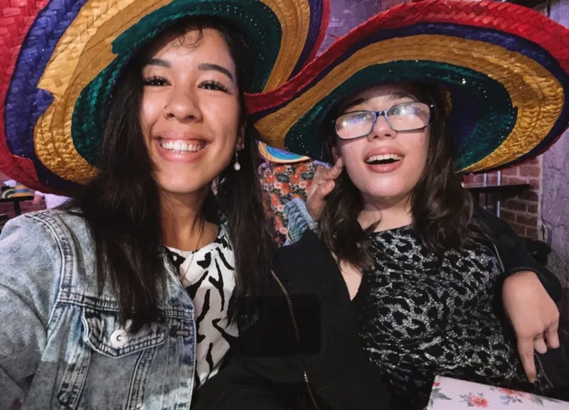 A participant and her support worker in oversized sombreros, grinning at a Mexican restaurant table